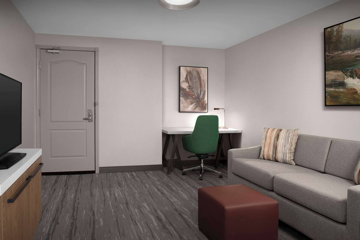 Ein modernes Hotelzimmer mit Flachbildfernseher, Schreibtisch mit Stuhl, einer Couch und einem Bild an der Wand.