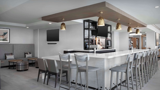 A modern bar area with a long counter, multiple stools, and pendant lighting. - Hilton Garden Inn Casper (Casper)