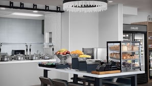 A modern kitchen area with a central island, bar stools, a refrigerator labeled "CHILLED," and various food items displayed. - Hilton Garden Inn Casper (Casper)