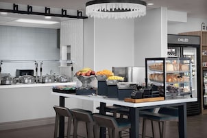 Una cocina moderna con una isla central, taburetes de bar, un refrigerador con la etiqueta 'CHILLED' y diversos alimentos a la vista.