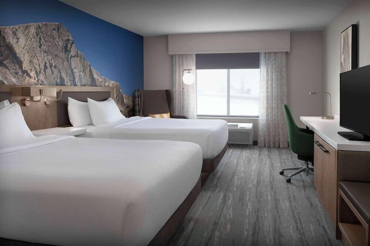 Ein Hotelzimmer mit zwei Betten, einem Schreibtisch, einem Stuhl, einem Fernseher und einem großen Fenster mit Vorhängen.