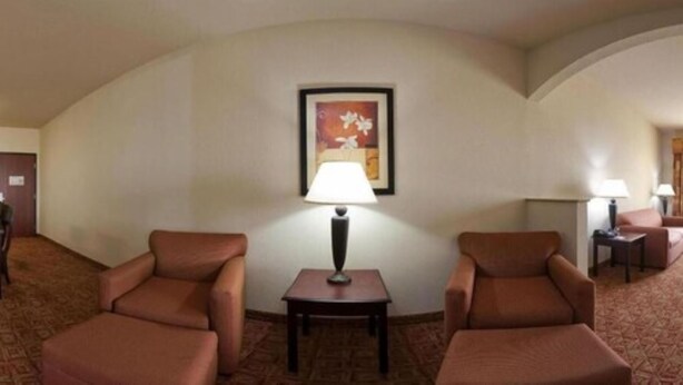Una habitación de hotel con dos sillones marrones, una mesita con una lámpara y un cuadro en la pared.
