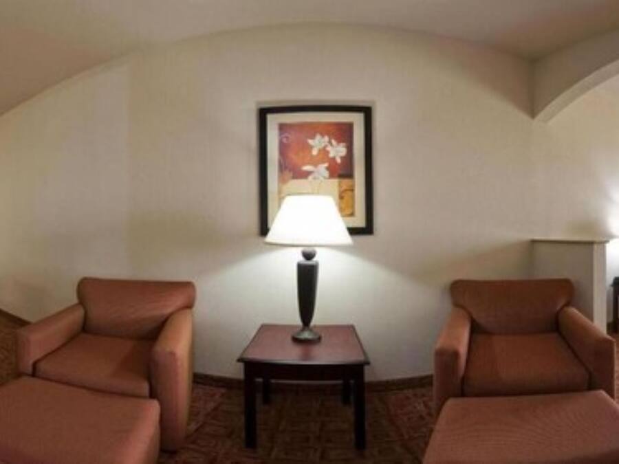 Una habitación de hotel con dos sillones marrones, una mesita con una lámpara y un cuadro en la pared.