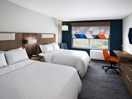 A hotel room with two beds, a desk, a chair, a TV, and a window with a view.