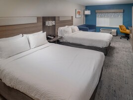 A hotel room with two beds, a desk, a chair, a lamp, and a window with blinds.