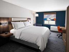 A hotel room with a large bed, bedside table, lamp, and a desk with an orange chair.