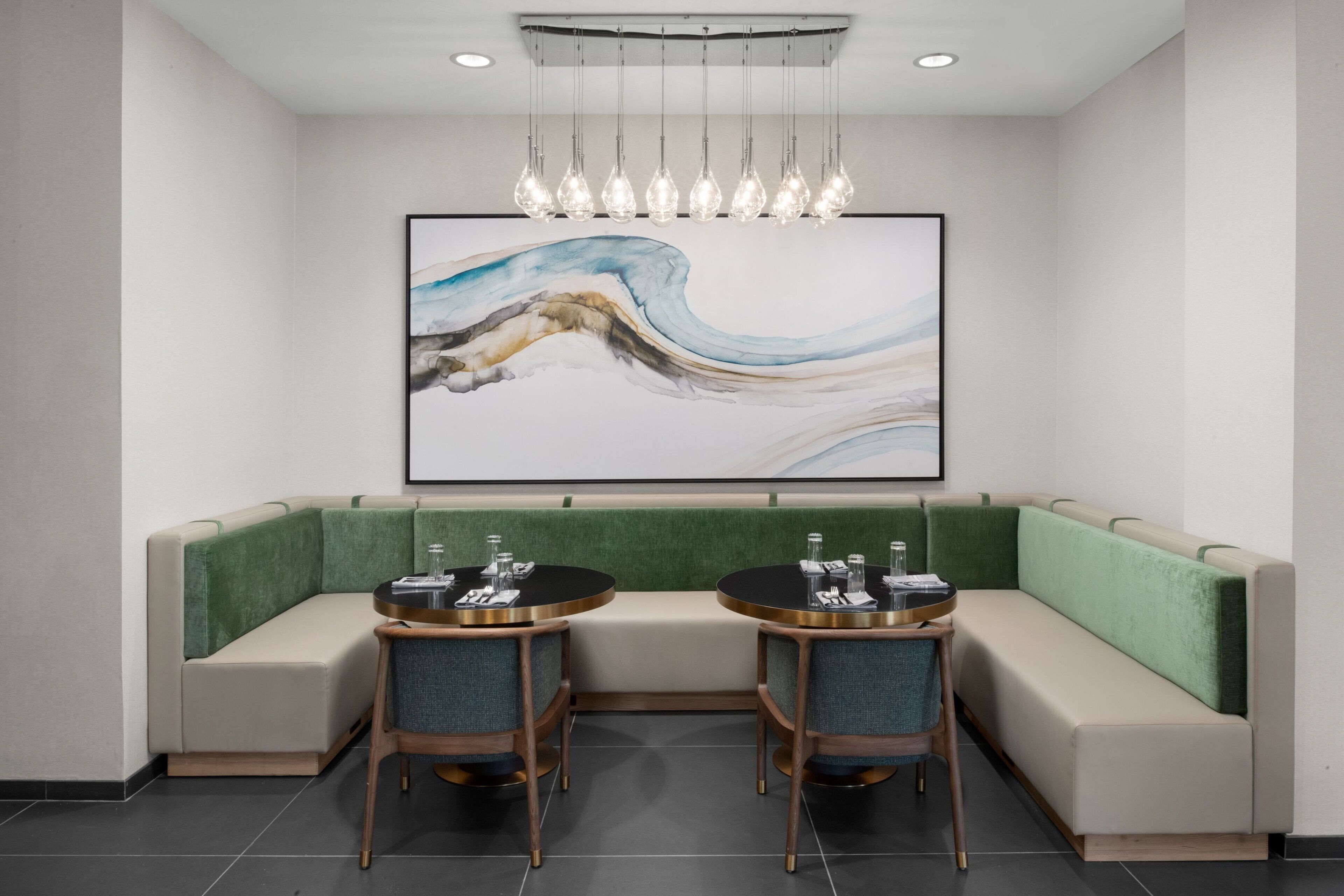Una sala de conferencias moderna con un banco acolchado verde, dos mesas redondas con sillas y un cuadro abstracto grande en la pared.