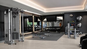 Un gimnasio moderno con varios equipos de ejercicio, espejos y un zapatero en la pared.