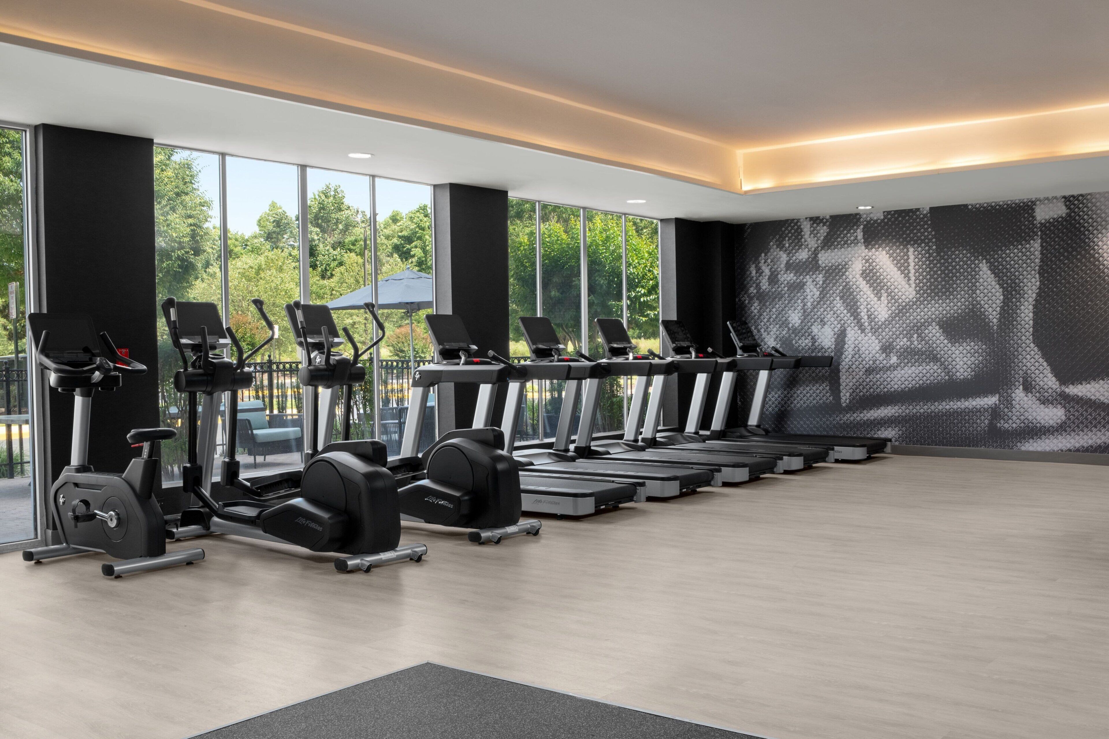 Un gimnasio moderno con cintas de correr, elípticas y pesas libres dispuestas en filas.