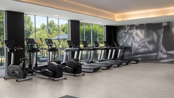Un gimnasio moderno con cintas de correr, elípticas y pesas libres dispuestas en filas.