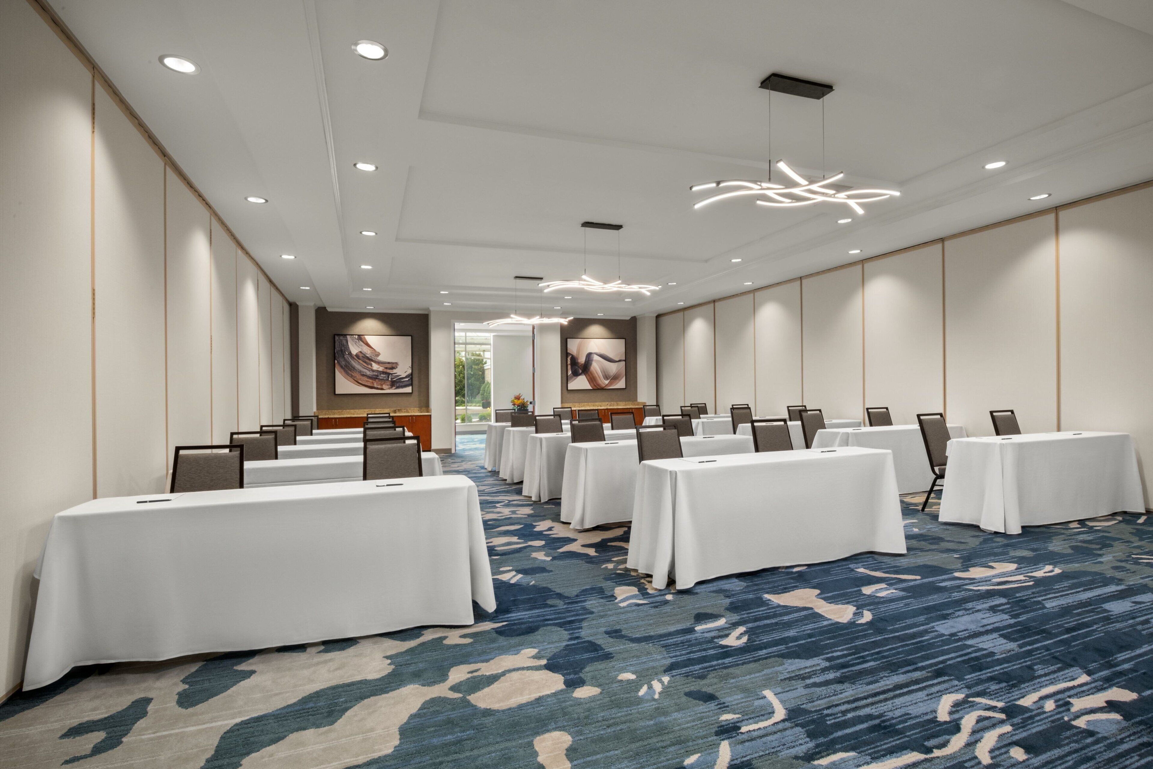 A conference room with multiple tables, white tablecloths, and a blue patterned carpet.