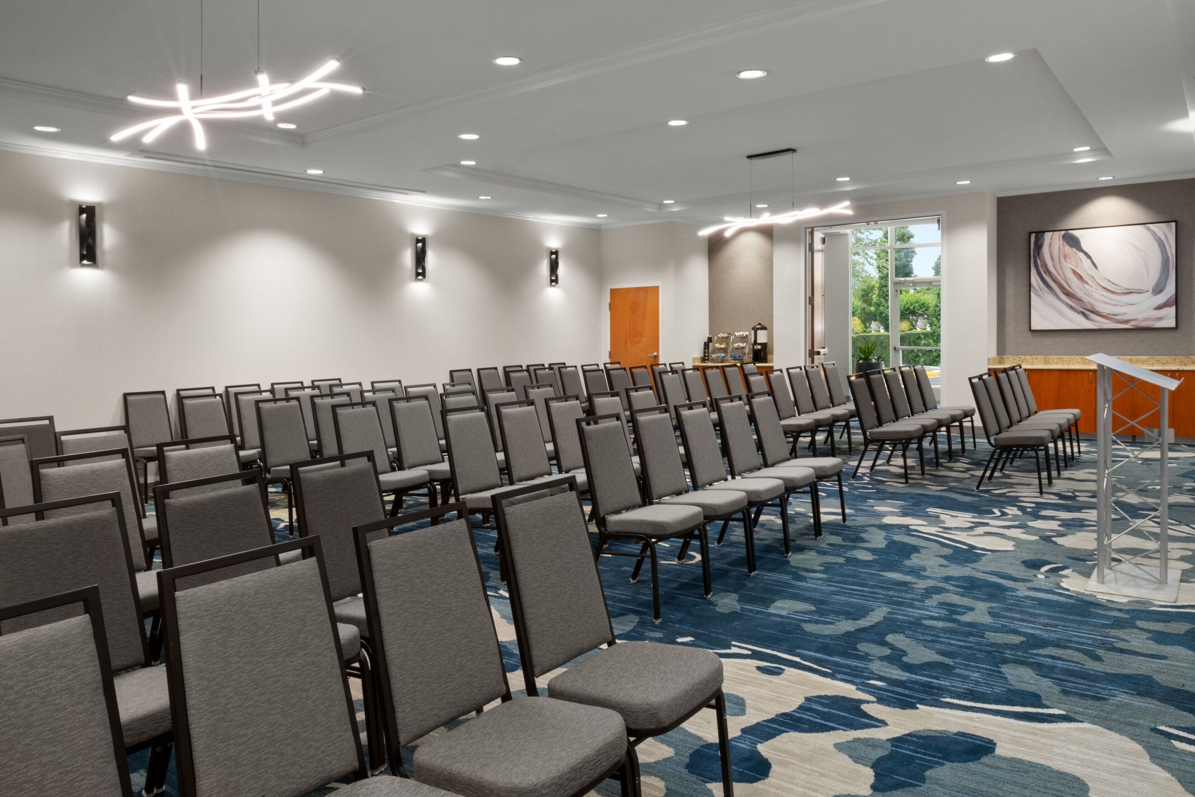 A conference room with rows of chairs, a podium, and a large window.