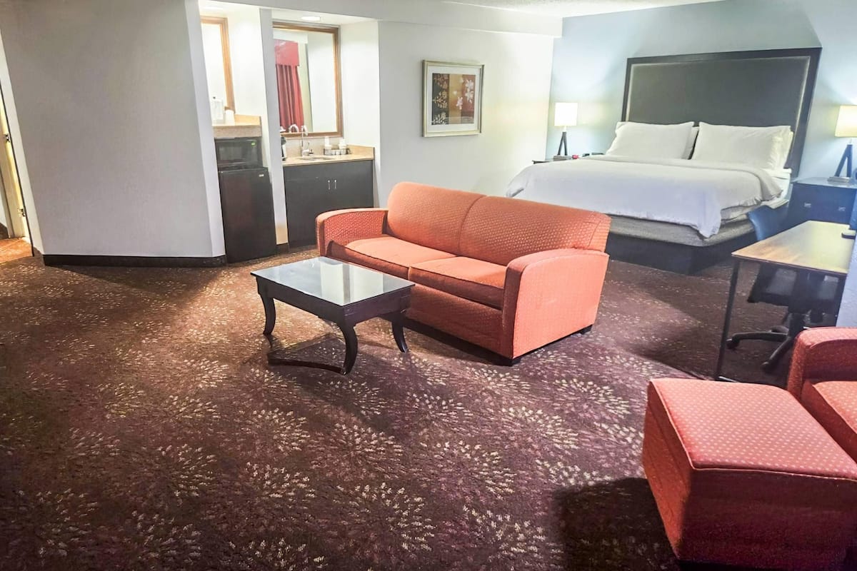 A hotel room with a bed, a sofa, a coffee table, a desk, and a kitchenette.