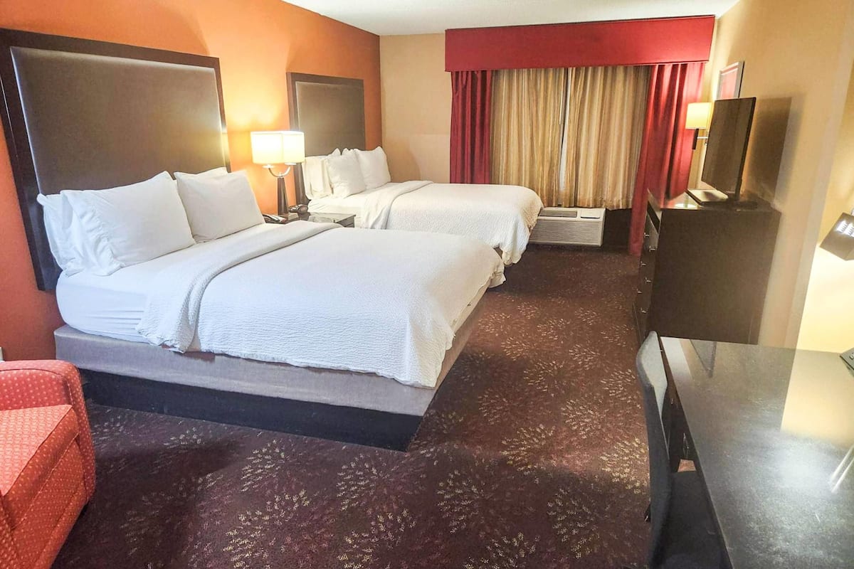 A hotel room with two beds, a TV, a desk, and a red armchair.