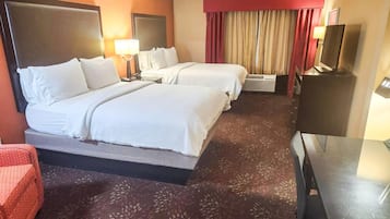 Une chambre d’hôtel avec deux lits, une télévision, un bureau et un fauteuil rouge.