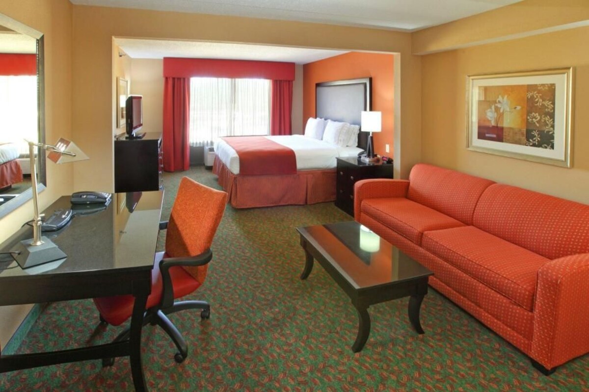 A hotel room with a bed, a sofa, a desk with a chair, a TV, and a lamp.