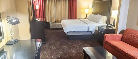 Une chambre d’hôtel avec un lit, un canapé, un bureau, une lampe, un miroir et un rideau rouge.