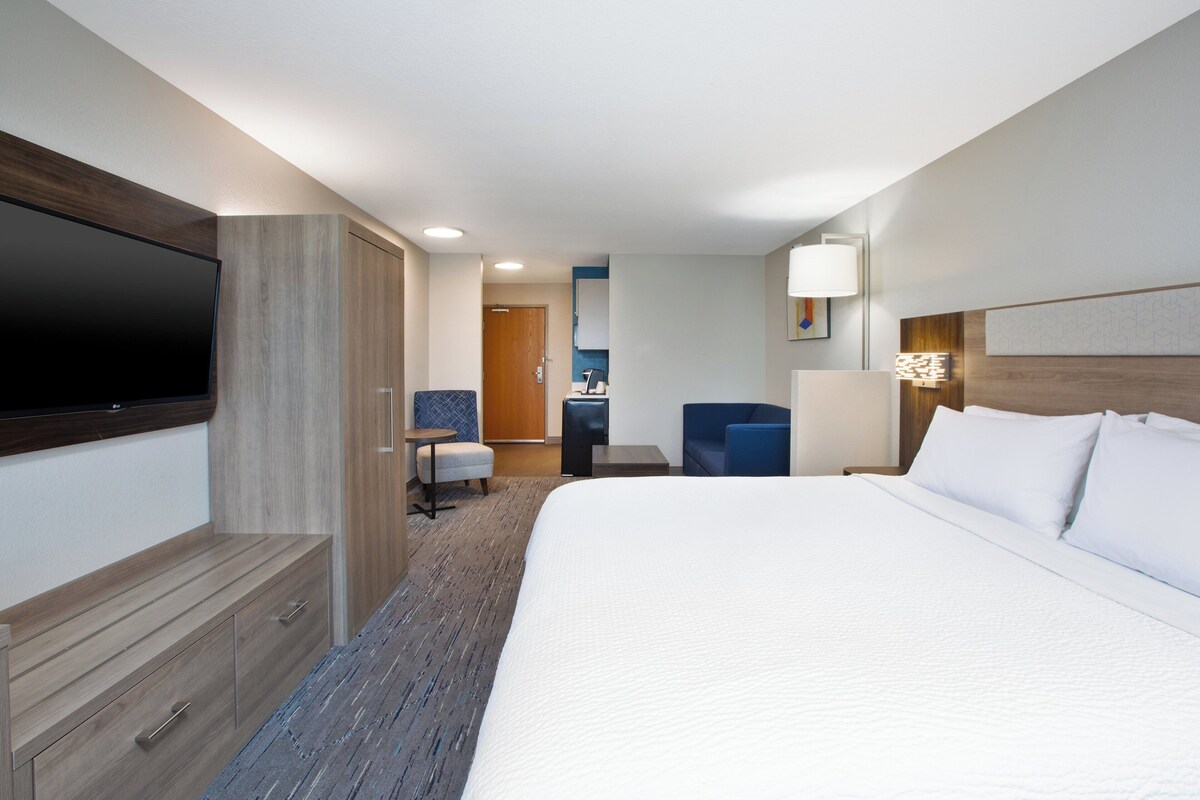 A hotel room with a large bed, a flat-screen TV, a desk with a chair, and a small seating area.