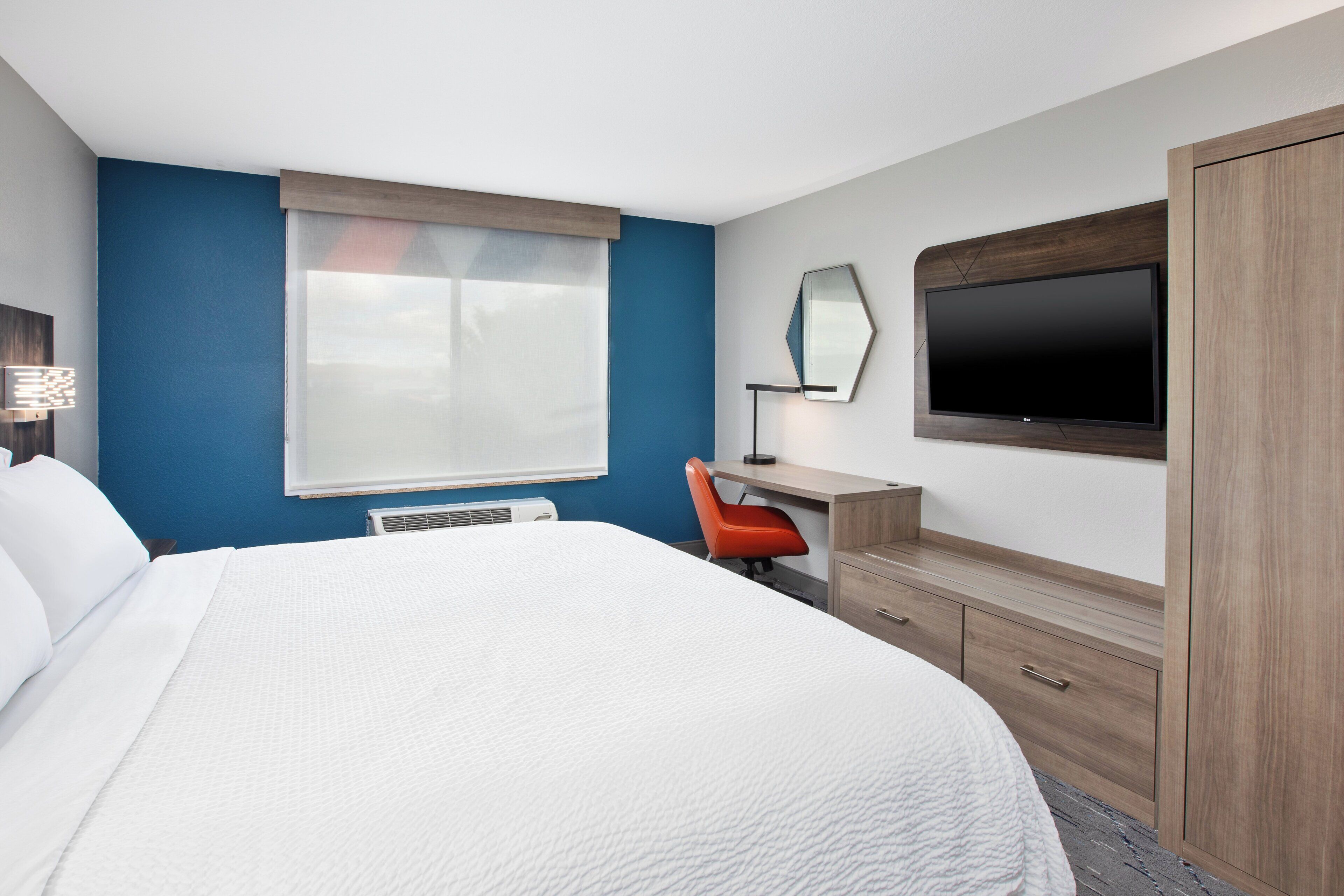 A hotel room with a bed, a desk, a chair, a television, and a wardrobe.