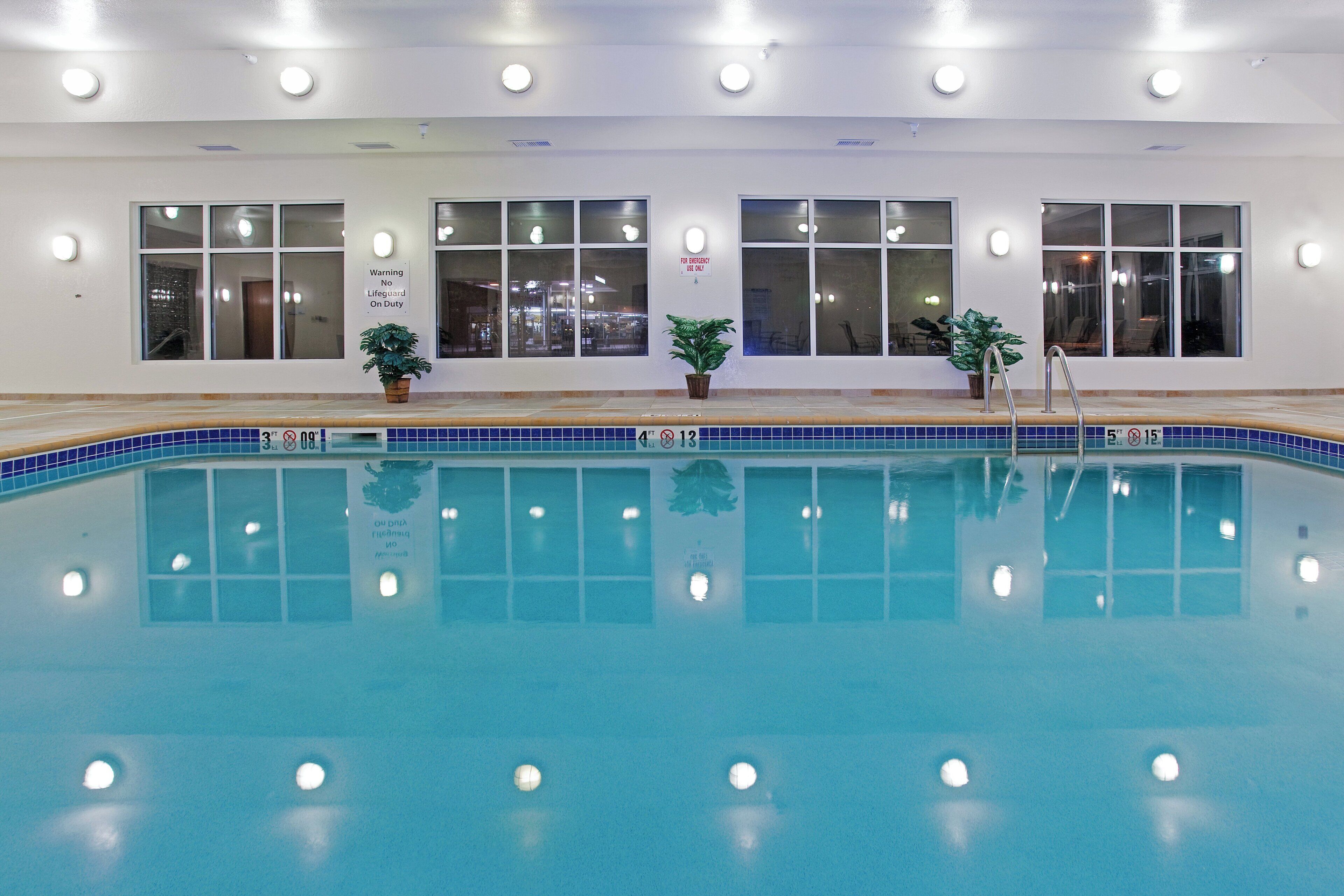 An indoor swimming pool with clear water, surrounded by windows and potted plants.