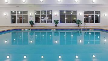 An indoor swimming pool with clear water, surrounded by windows and potted plants.