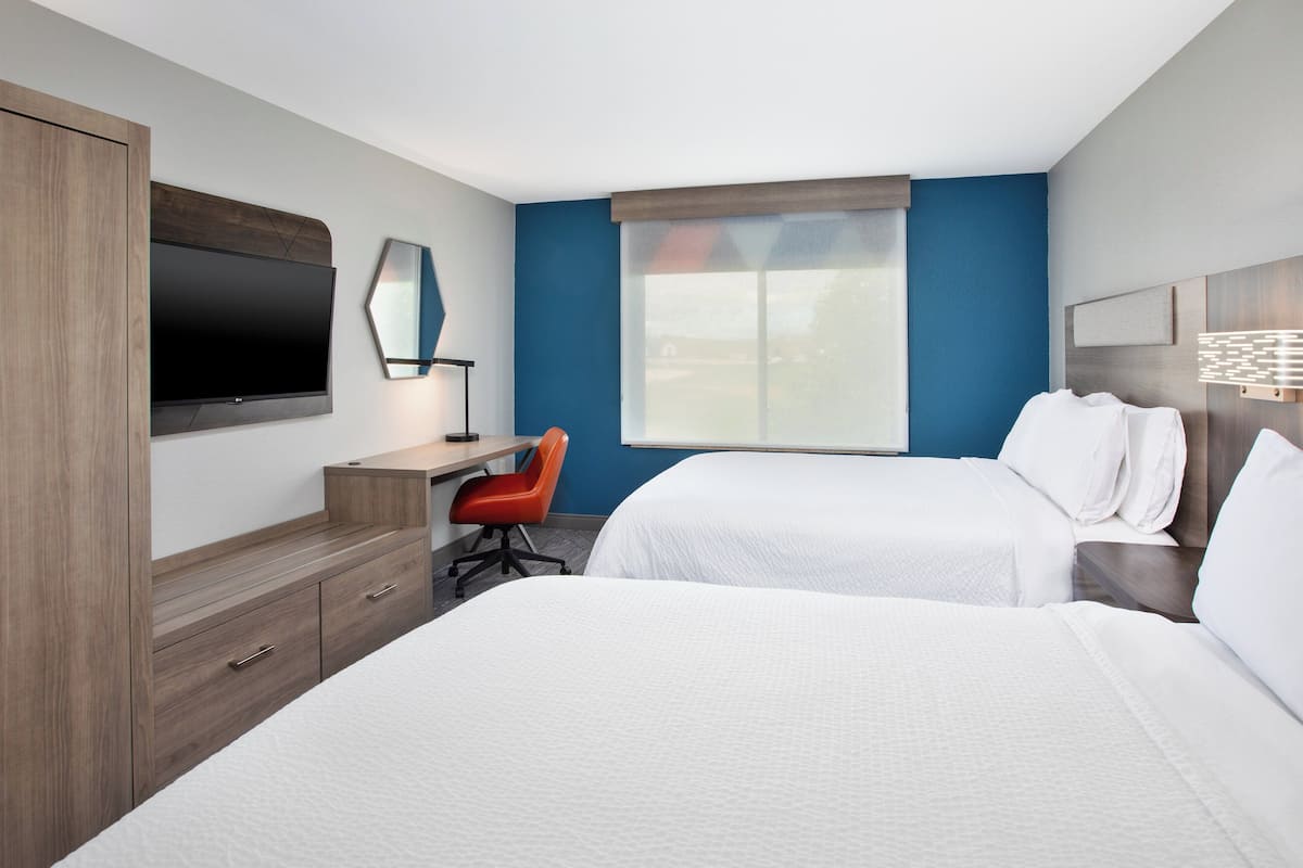 A hotel room with two beds, a desk, a chair, a TV, and a window with a view.