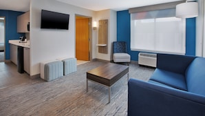 Une chambre d’hôtel moderne équipée d’une télévision à écran plat, d’un canapé, d’une table basse, d’un petit coin salon et d’une fenêtre avec des stores.