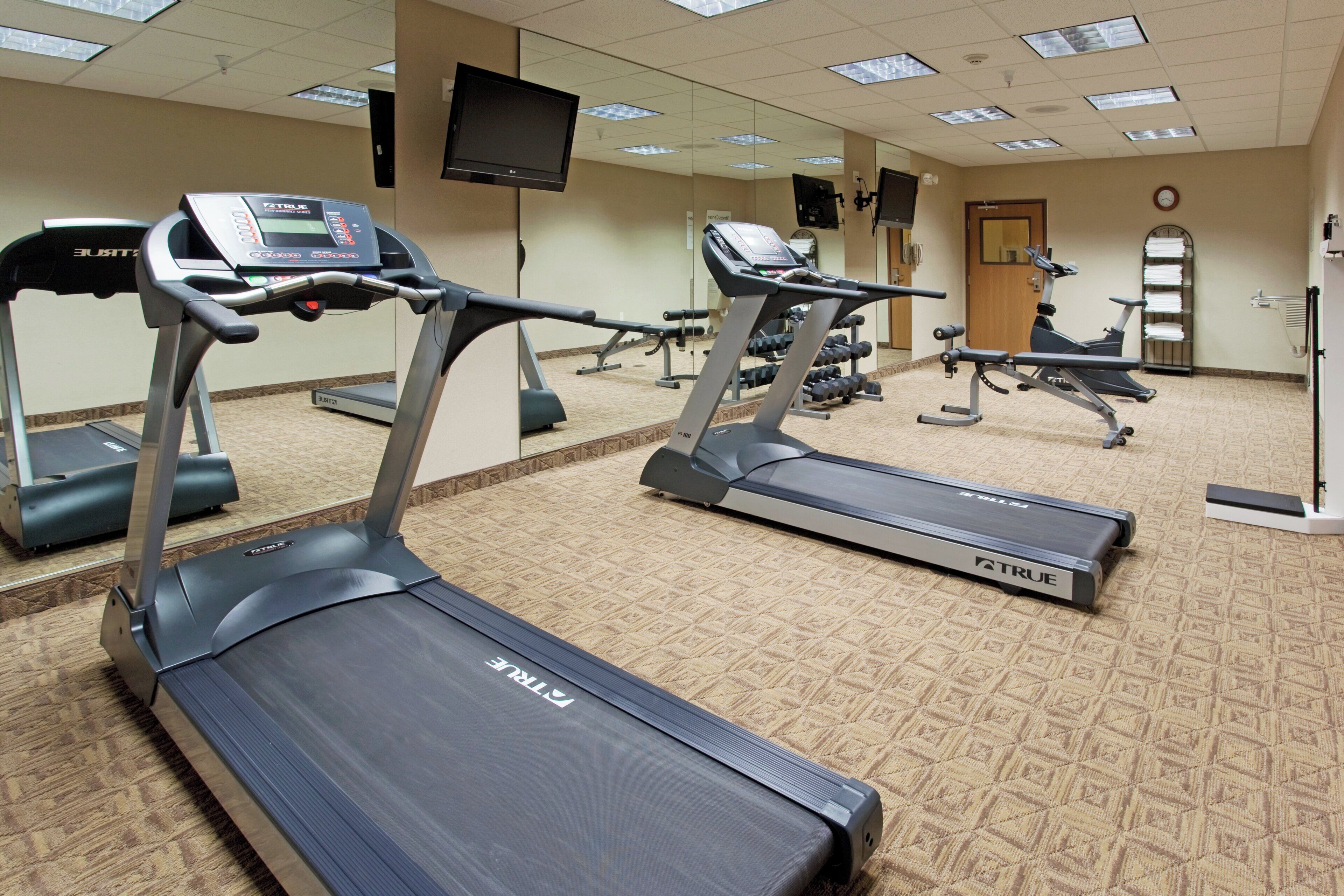 A fitness center with treadmills, weight machines, and a television on the wall.