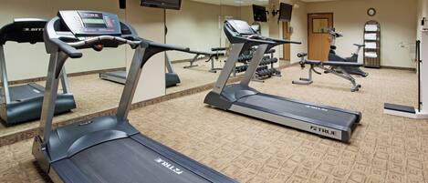 A fitness center with treadmills, weight machines, and a television on the wall.