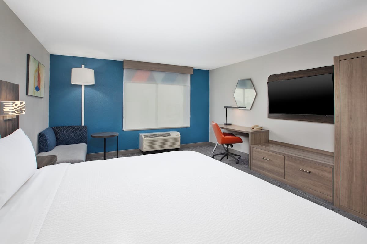 A hotel room with a large bed, a desk with a chair, a flat-screen TV, and a wardrobe.