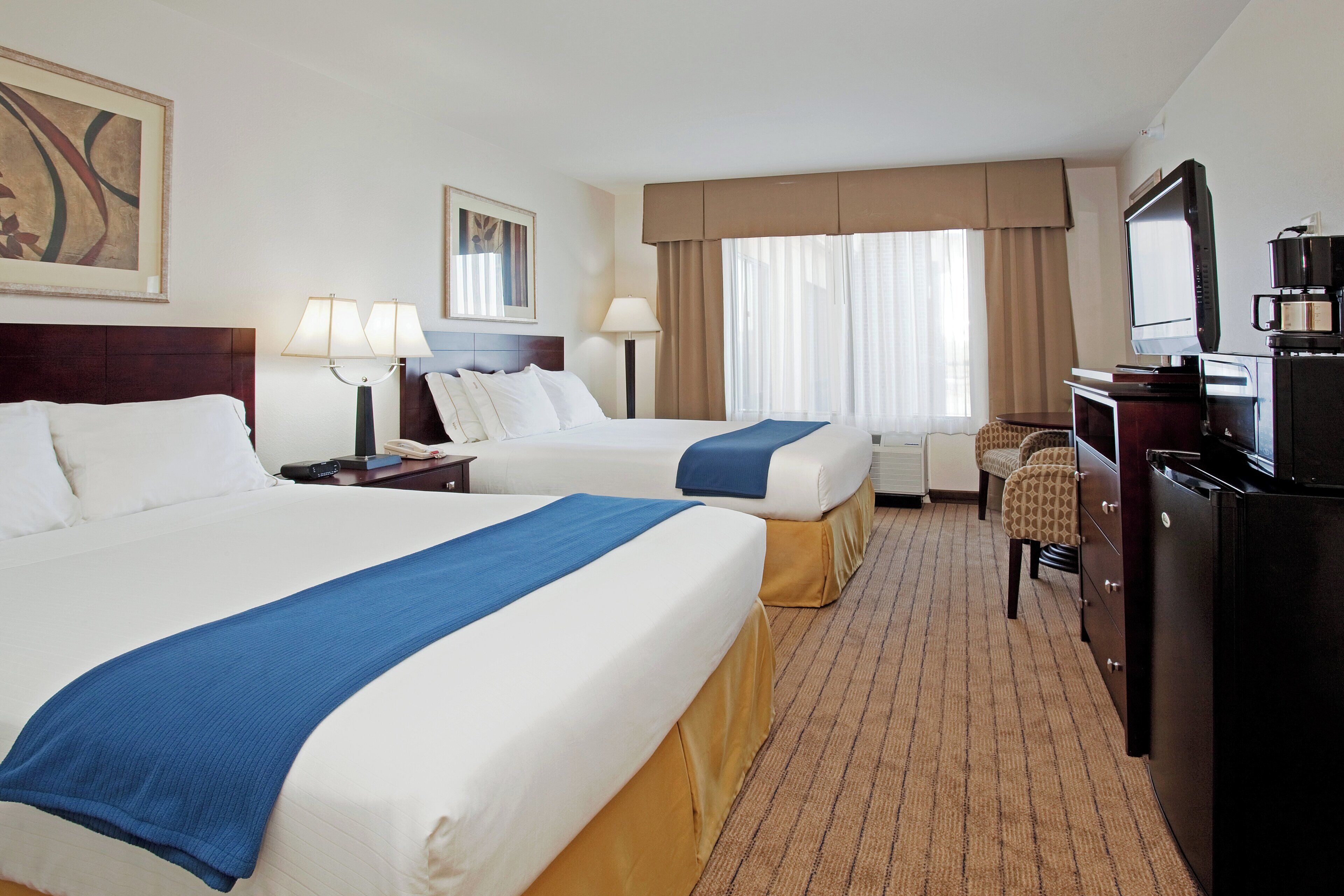 Habitación de hotel con dos camas, televisión, escritorio con computadora y ventana con cortinas.