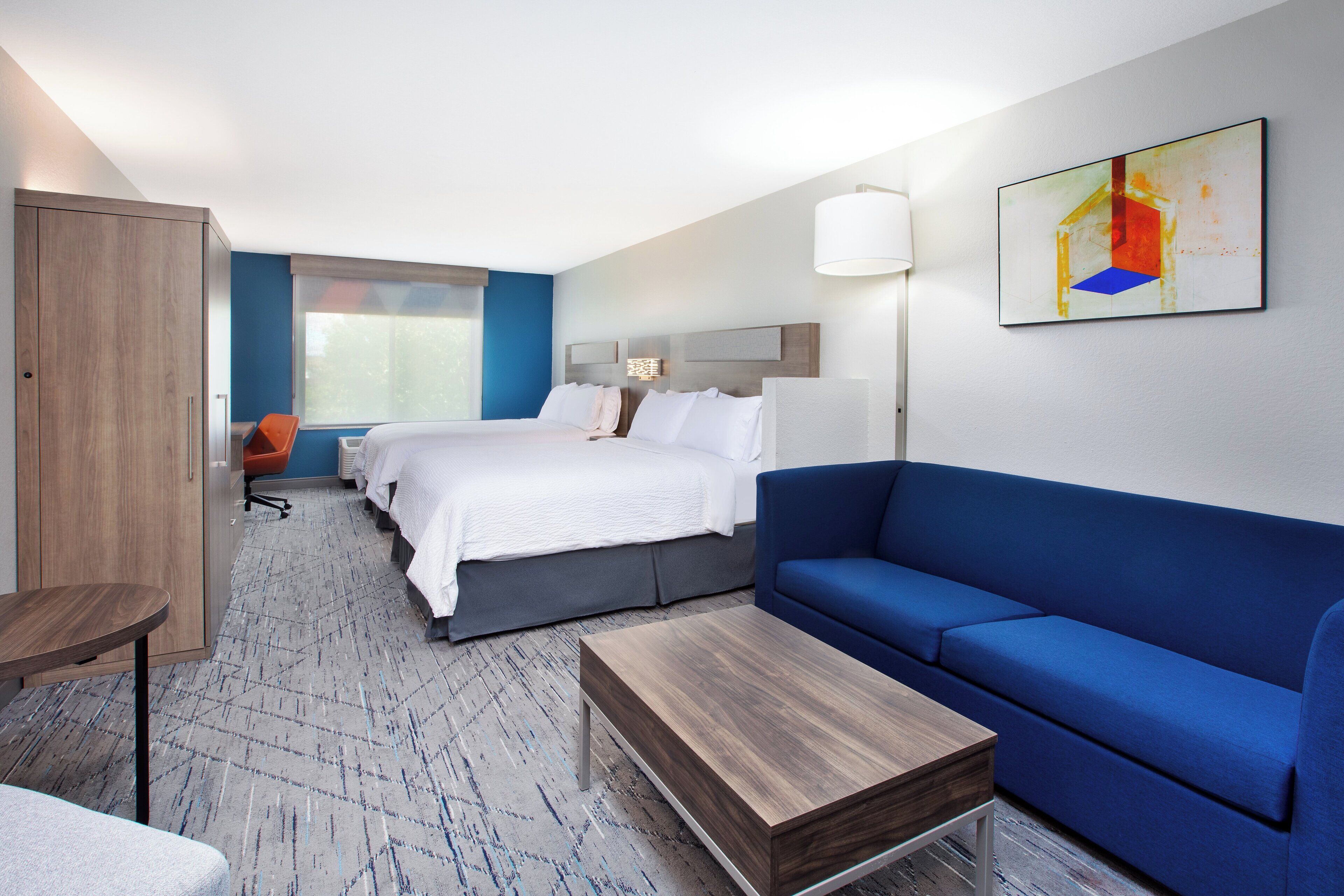 Une chambre d’hôtel avec un lit, un canapé bleu, une table basse en bois, un bureau et une chaise.