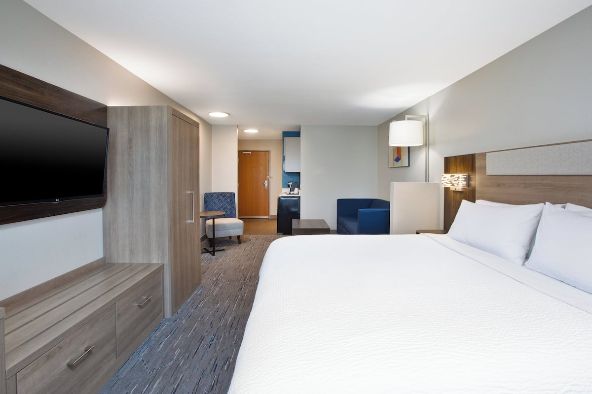 A hotel room with a large bed, a flat-screen TV, a desk with a chair, and a small seating area.