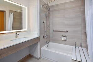 A modern bathroom with a bathtub, a shower, a vanity with a mirror, and a towel rack.