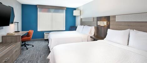 A hotel room with two beds, a desk, a chair, a TV, and a window.