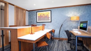 Une chambre d’hôtel avec un bureau en bois, deux chaises, un ordinateur et une lampe de bureau.