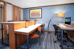 A hotel room with a wooden desk, two chairs, a computer, and a desk lamp.