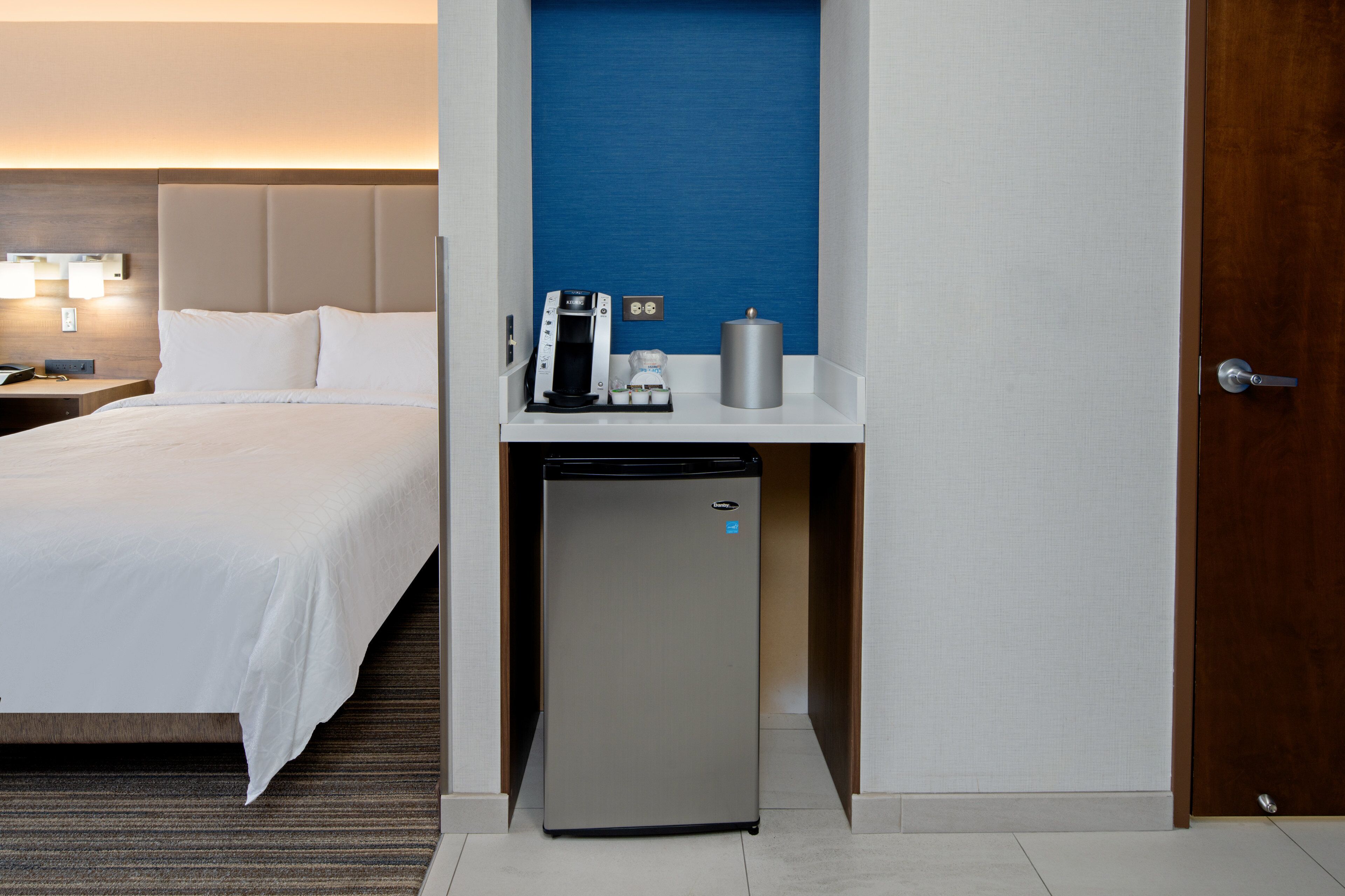 Une chambre d’hôtel équipée d’un lit, d’un petit réfrigérateur, d’une machine à café et d’une table de chevet.