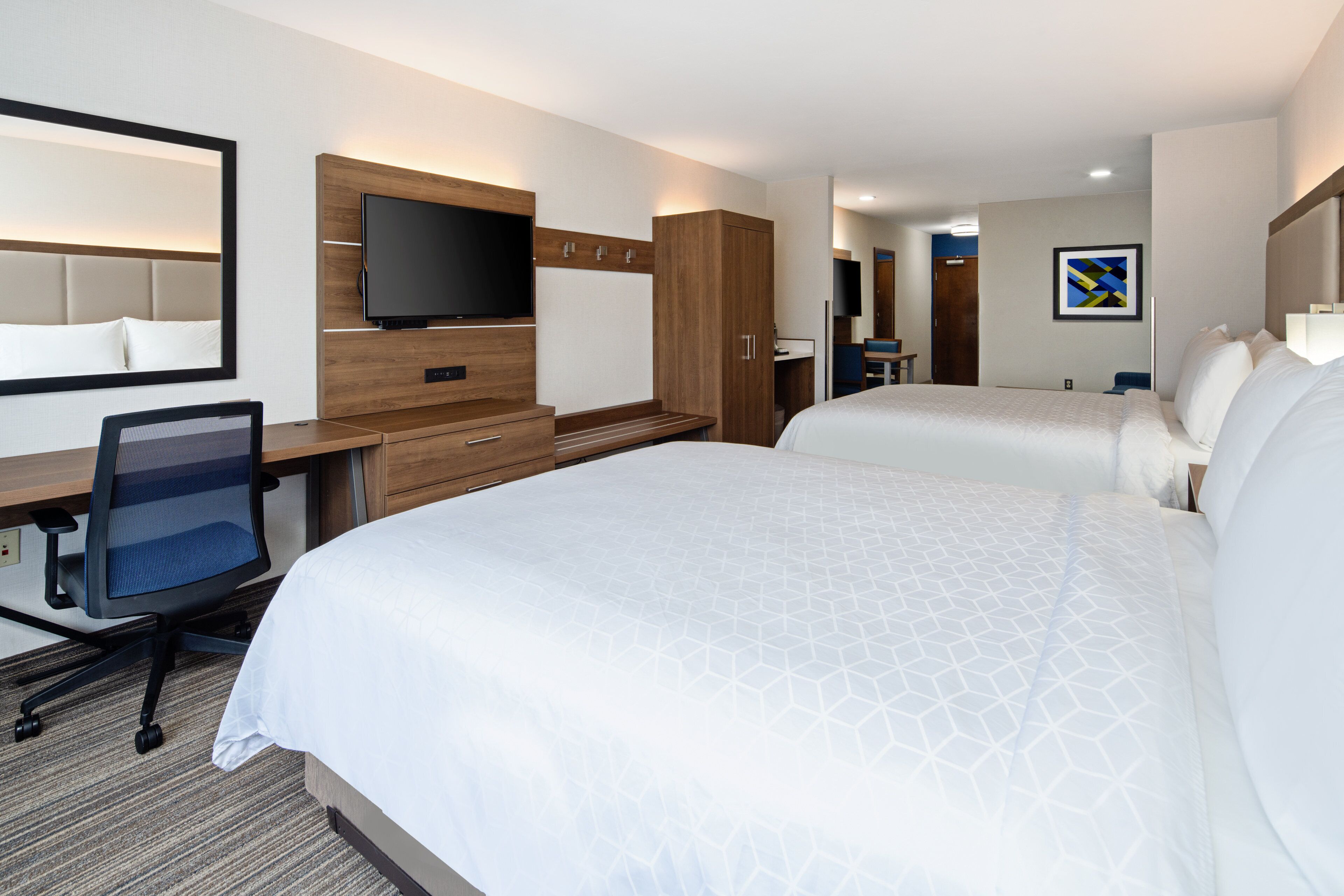 A hotel room with two beds, a desk with a chair, a TV, and a wooden cabinet.