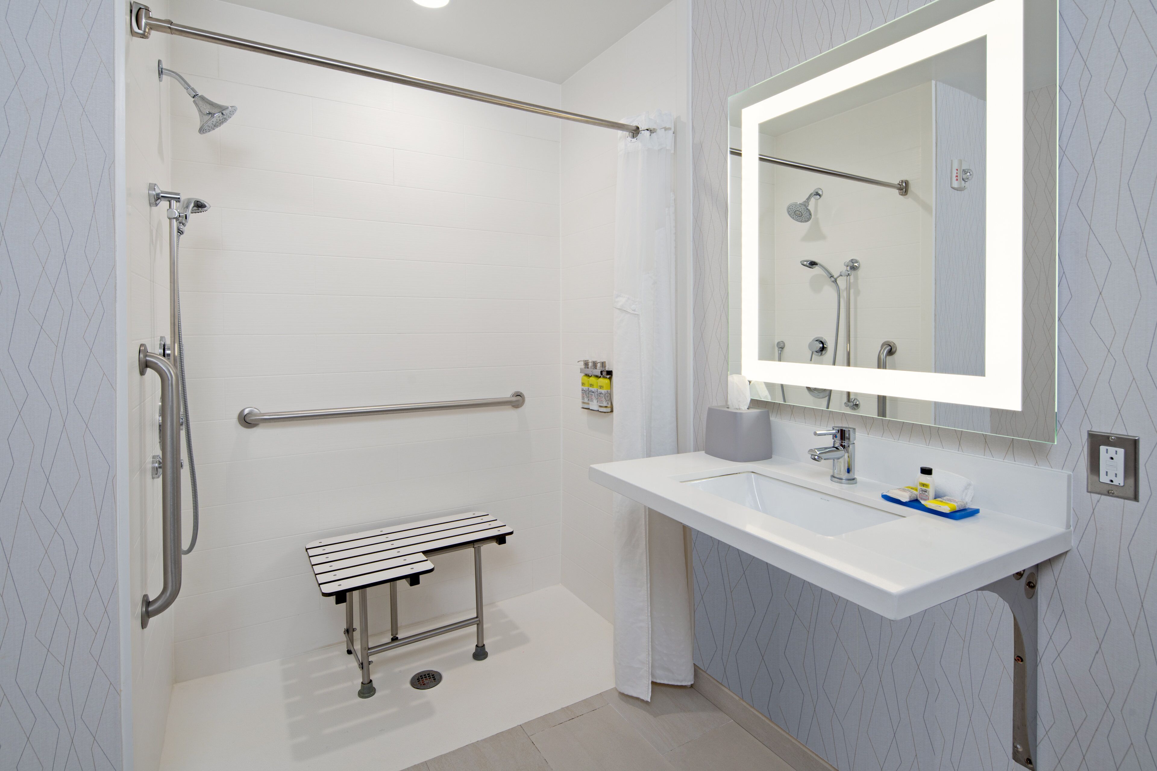 A modern bathroom with a shower, grab bar, bench, and sink with a mirror.
