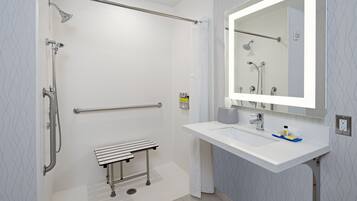 A modern bathroom with a shower, grab bar, bench, and sink with a mirror.