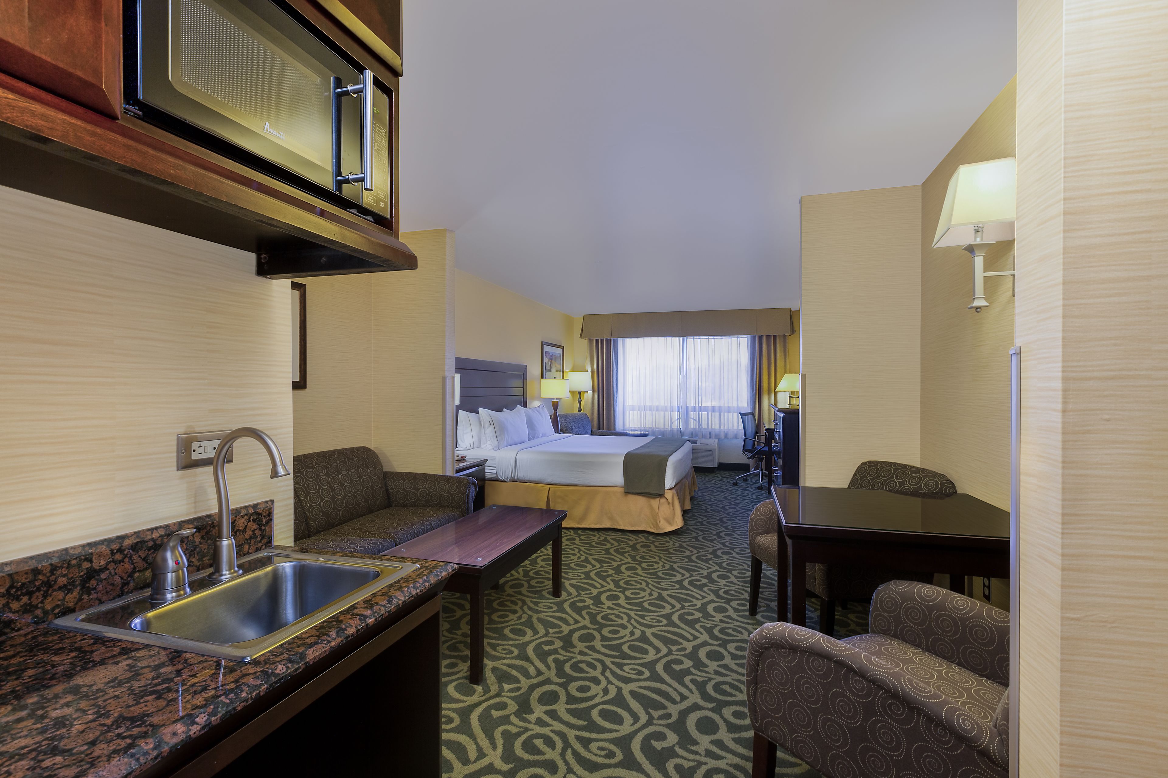 A hotel room with a kitchenette, a bed, a desk, and a chair.