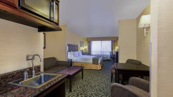 A hotel room with a kitchenette, a bed, a desk, and a chair.