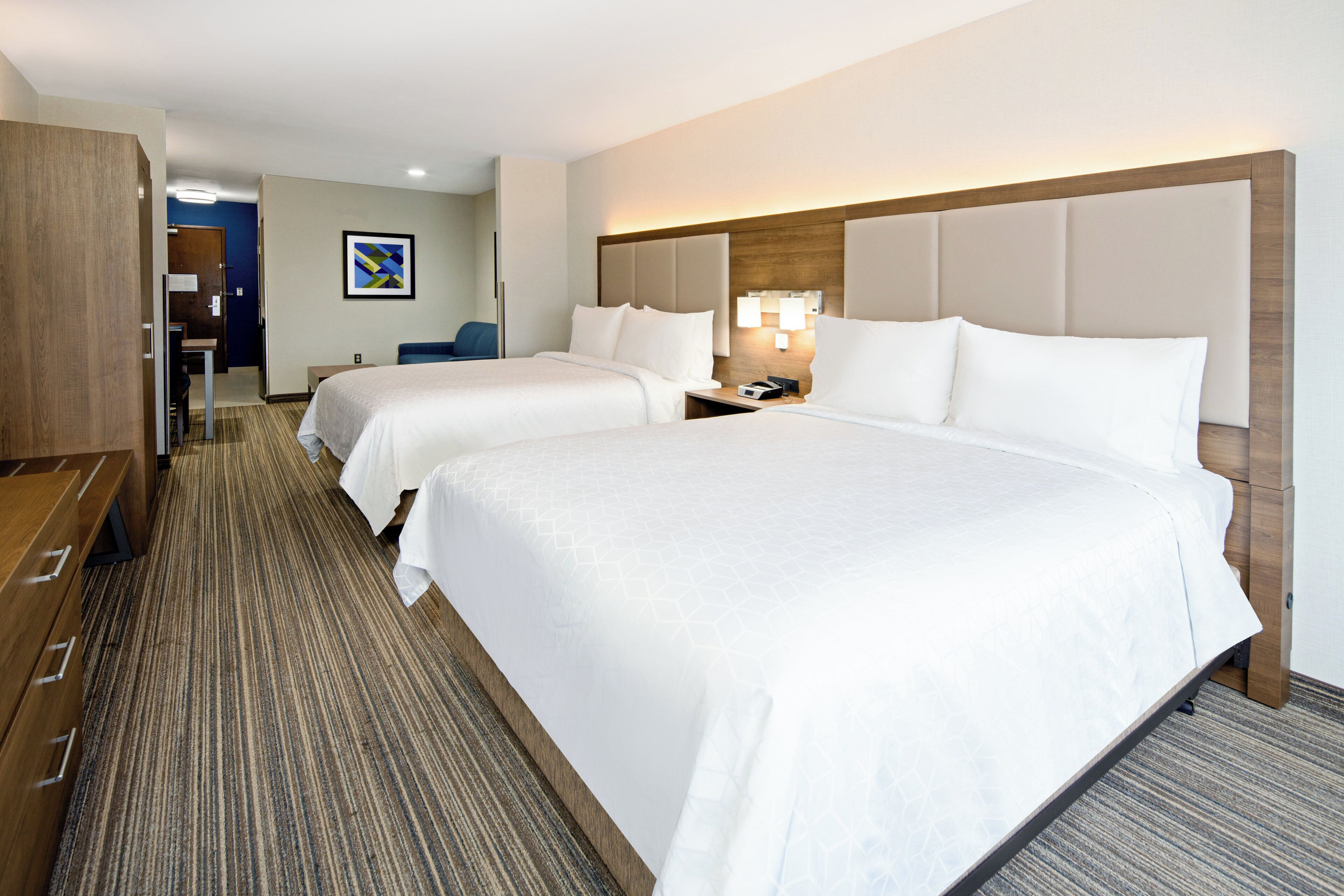 Een hotelkamer met twee bedden, een bureau, een stoel en een houten garderobe.