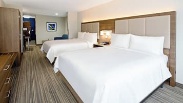 A hotel room with two beds, a desk, a chair, and a wooden wardrobe.
