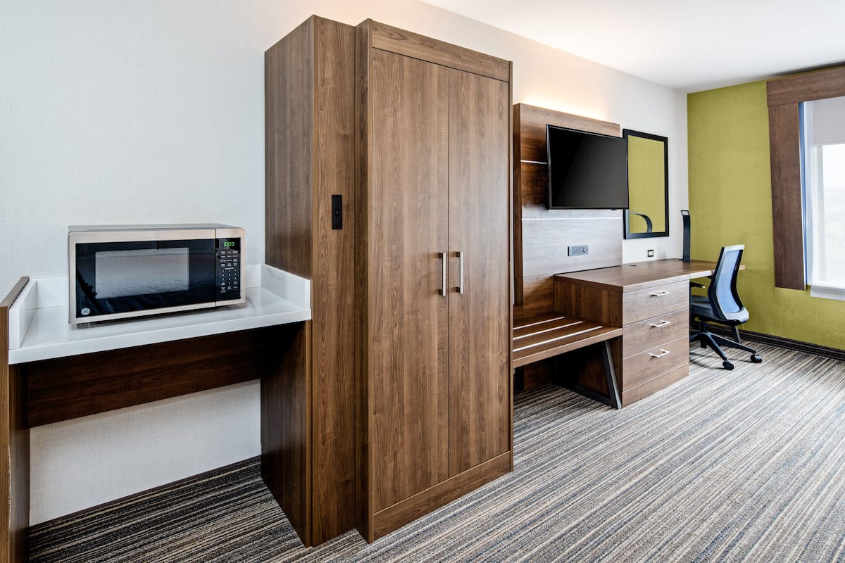 Ett hotellrum med en garderob i trä, en mikrovågsugn, ett skrivbord med lådor, en stol, en platt-TV och ett fönster med utsikt.