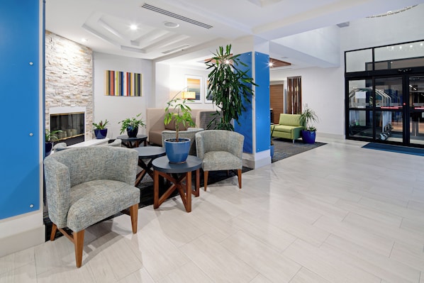 A modern lobby with seating, a fireplace, and potted plants.