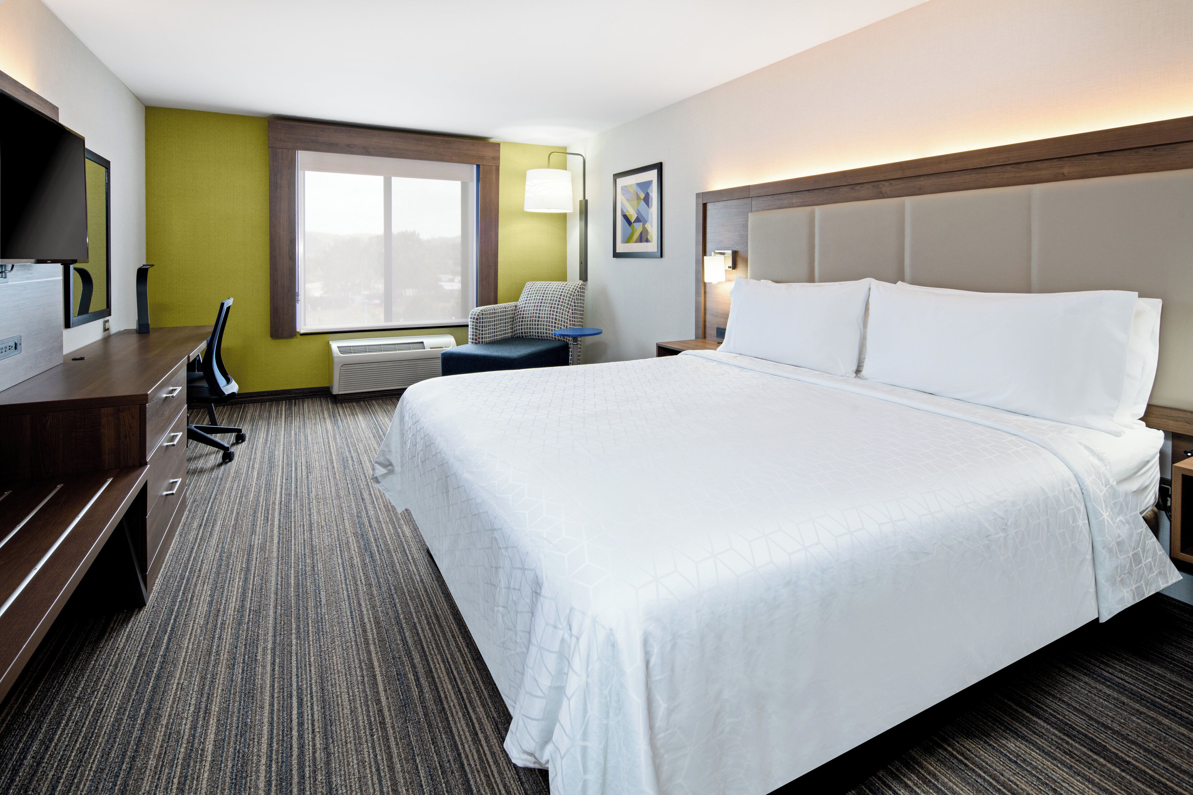 Ein Hotelzimmer mit einem großen Bett, einem Schreibtisch, einem Sessel, einem Fenster und einem Fernseher.