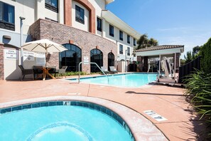 A swimming pool area with a brick building, lounge chairs, and a covered seating area.