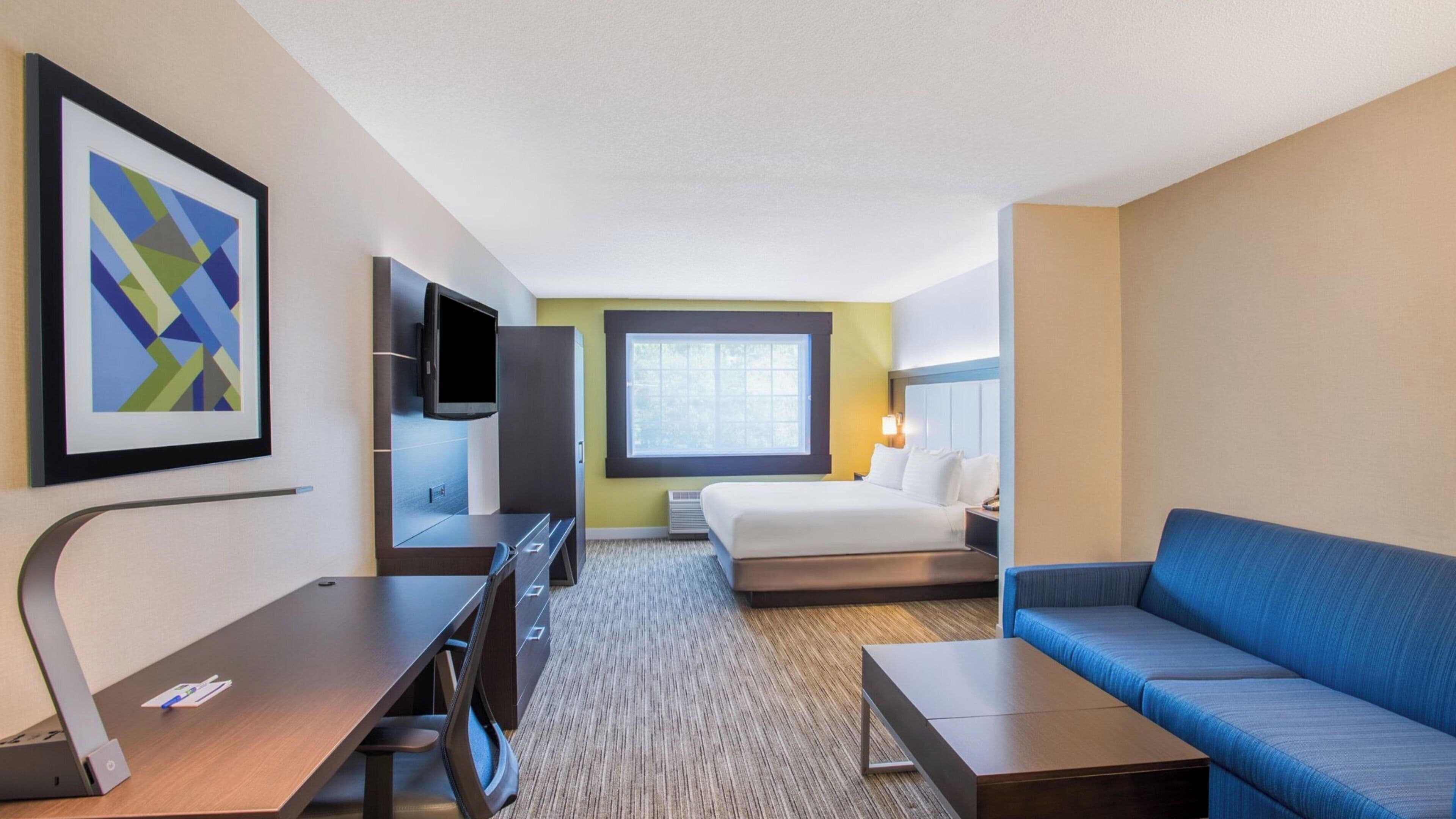 Quarto de hotel com cama, escrivaninha, televisão, sofá e janela.
